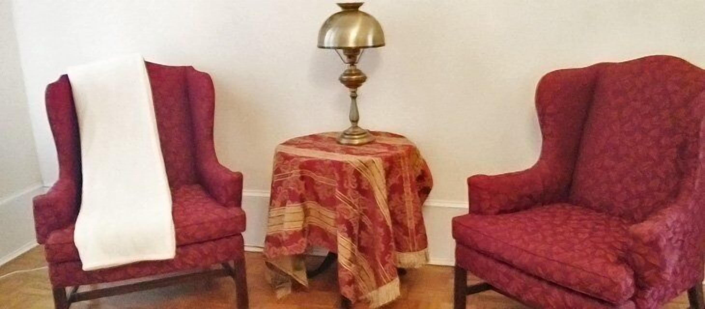 Two red armchairs with a patterned throw, a small round table with a lamp, and a white throw blanket on one chair.