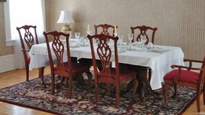 A dining area with a table set for six, surrounded by six wooden chairs with red cushions. - The Confederate House (Savannah)