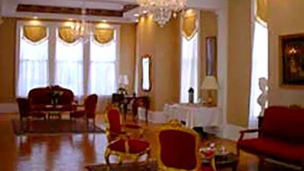 A spacious lobby with a chandelier, red and gold furniture, and large windows. - The Confederate House (Savannah)