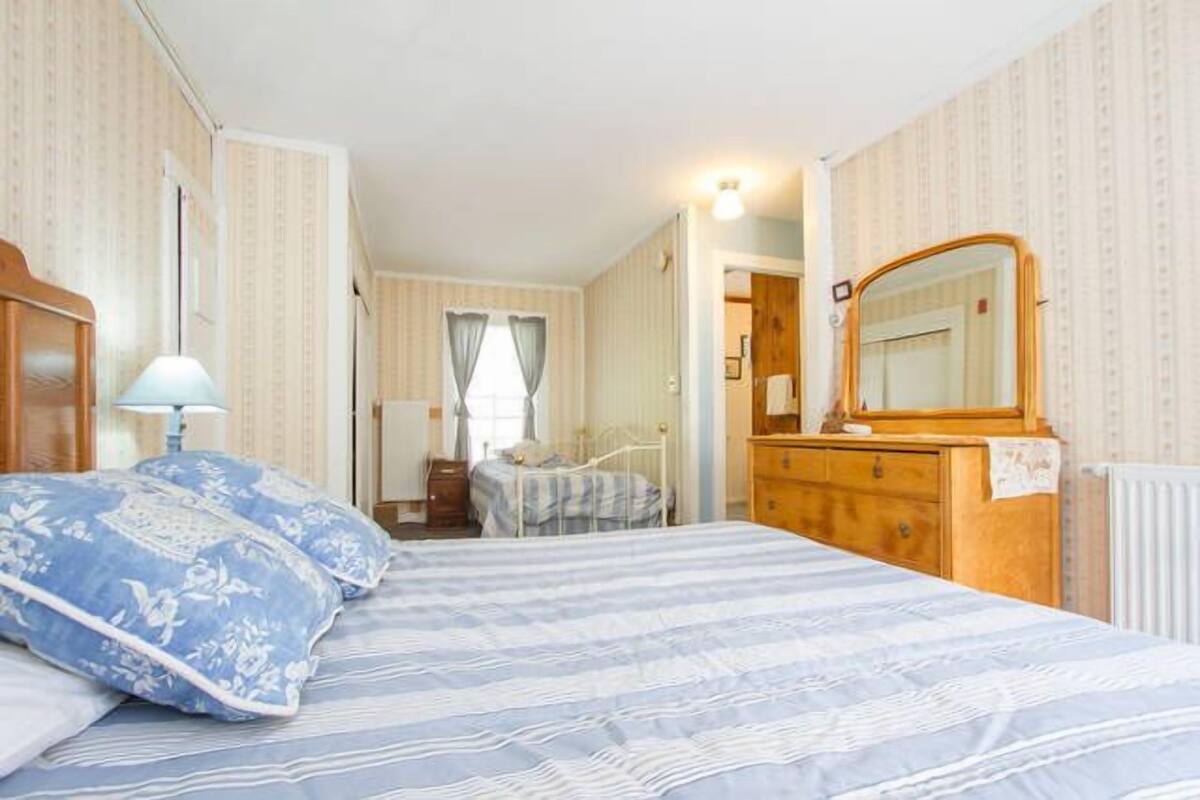A bedroom with a bed, a dresser, a mirror, and a window with curtains.