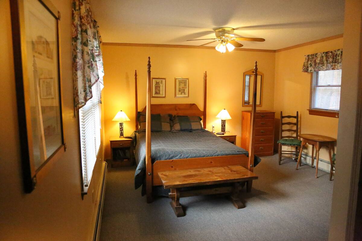 A bedroom with a four-poster bed, a wooden bench, a desk, and a chair.