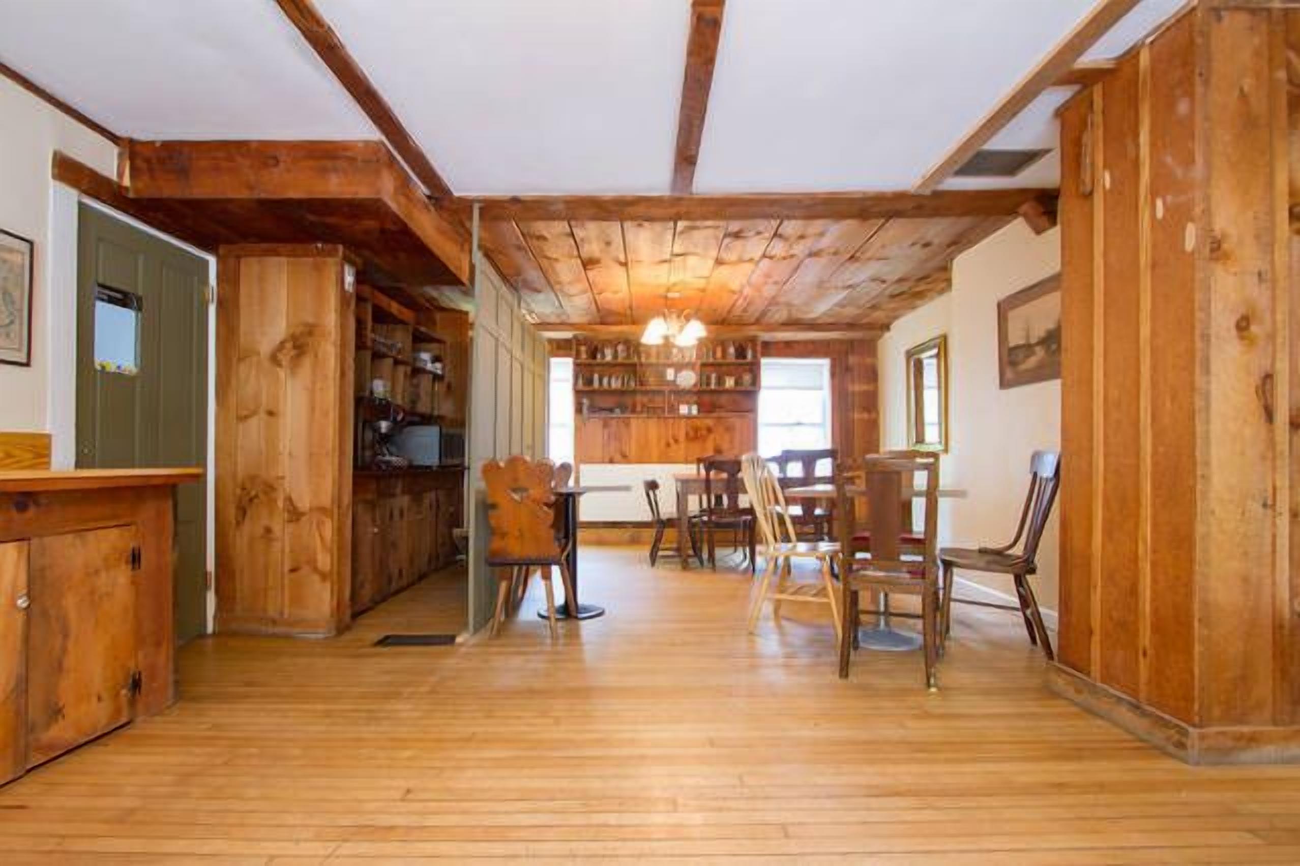 A spacious room with wooden floors, a dining area with chairs and a table, and a bookshelf filled with books.