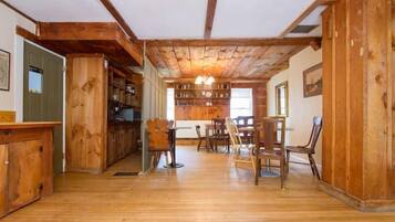 A spacious room with wooden floors, a dining area with chairs and a table, and a bookshelf filled with books.