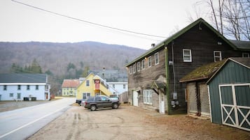 A rural road with a parked SUV, a wooden building with a green door, and a yellow building with a red sign.