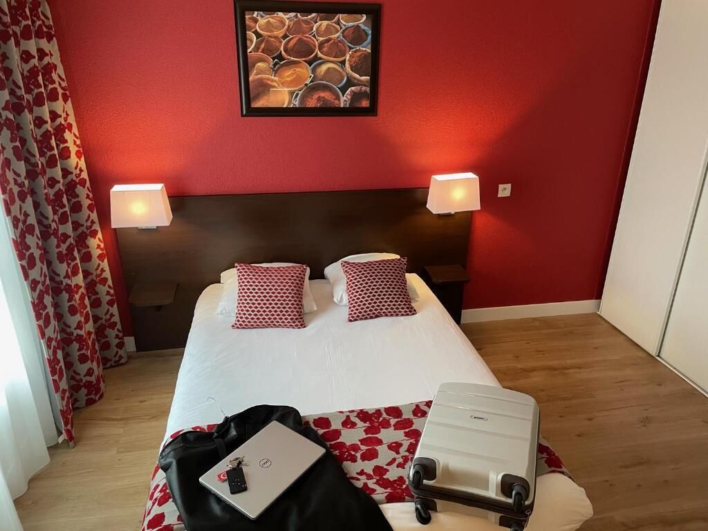 Een hotelkamer met een bed, twee bedlampjes, een ingelijste foto aan de muur en een koffer op de vloer.