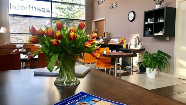 A dining area with a vase of tulips on a table, a magazine, and a clock on the wall. - Appartéa Grenoble Alpexpo (Grenoble)