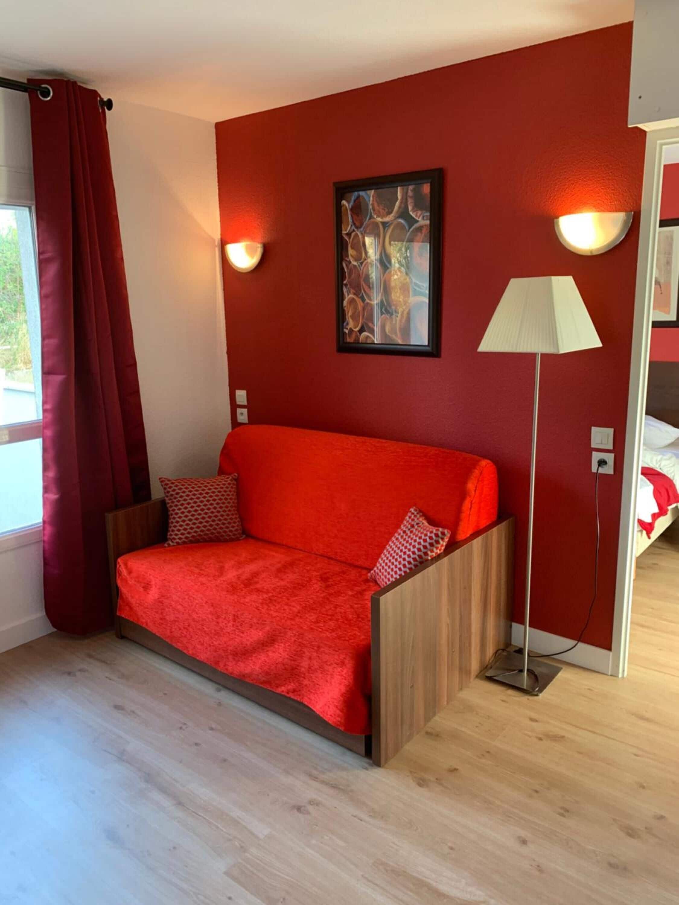 Una habitación con un sofá rojo, una lámpara y un cuadro en la pared.