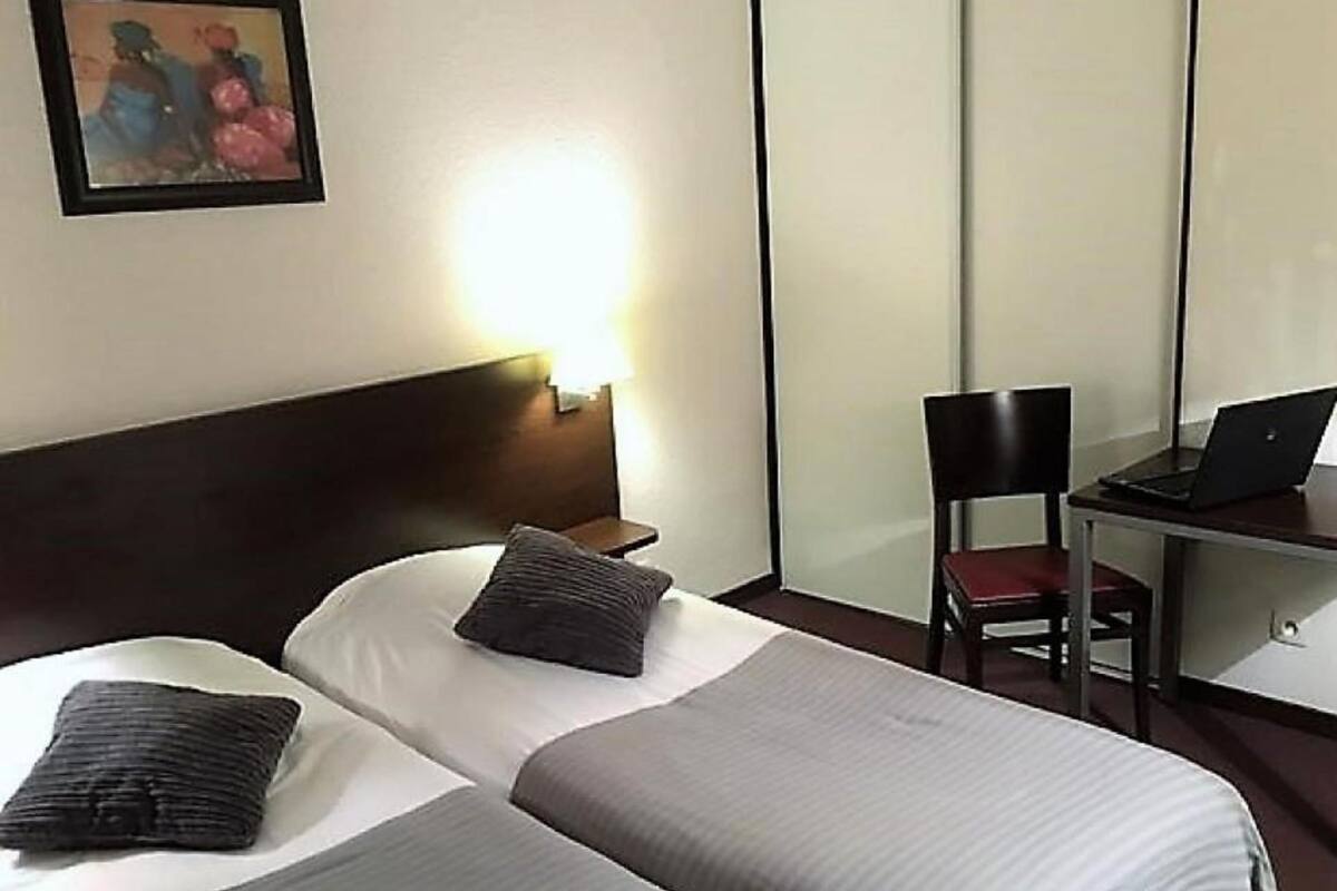 Ein Hotelzimmer mit einem Bett, einem Schreibtisch mit einem Laptop, einem Stuhl und einem Bild an der Wand.