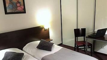 A hotel room with a bed, a desk with a laptop, a chair, and a painting on the wall.