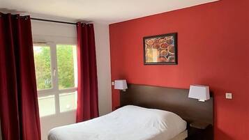 Ein Hotelzimmer mit einem Bett, roten Wänden, einem Fenster mit Vorhängen und einem Bild an der Wand.