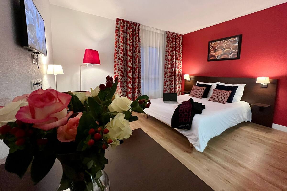Ein Hotelzimmer mit Bett, Schreibtisch, Fernseher und Blumenvase.