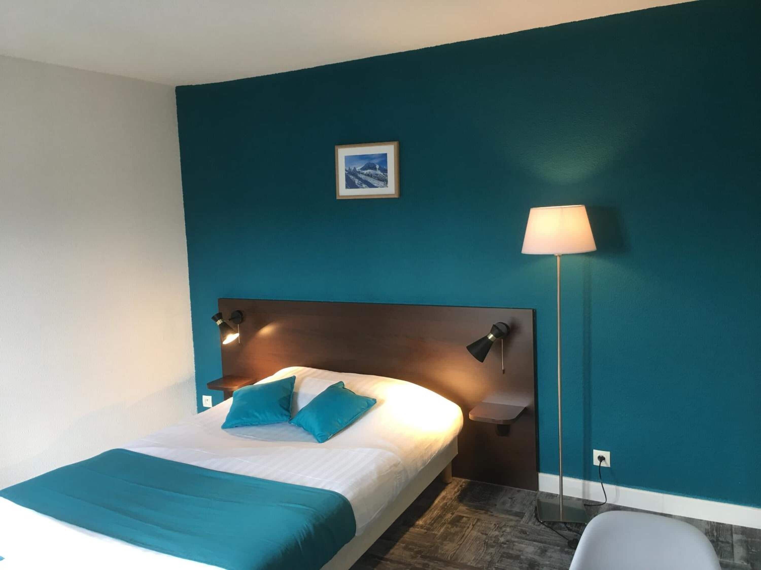 A hotel room with a bed, a nightstand, a lamp, and a picture on the wall.