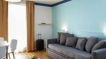 Een moderne woonkamer met een grijze bank, een klein rond tafeltje met fruit, een witte stoel, een zwarte koffer en een blauwe accentmuur.
