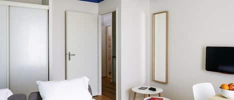Habitación de hotel con cama, escritorio, silla, mesita, televisor y frutero.