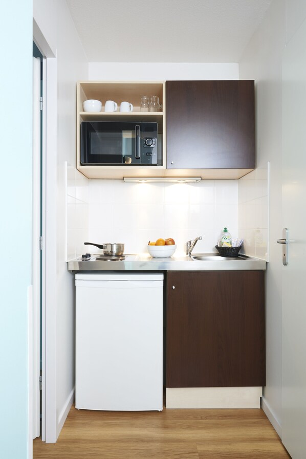 A compact kitchen with a microwave, sink, and a small refrigerator.