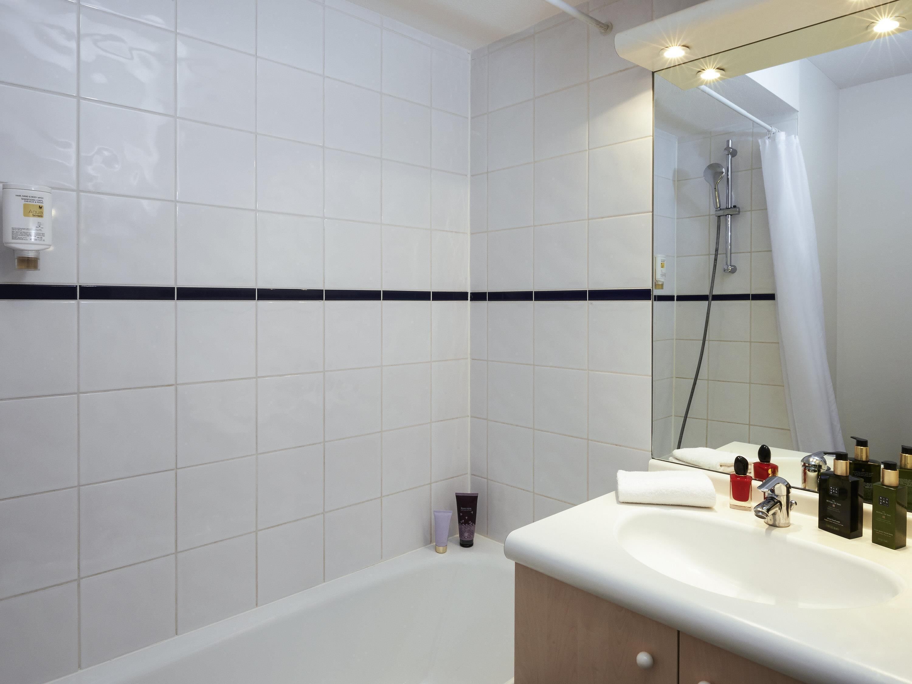 A bathroom with white tiles, a bathtub, a sink with toiletries, and a shower.