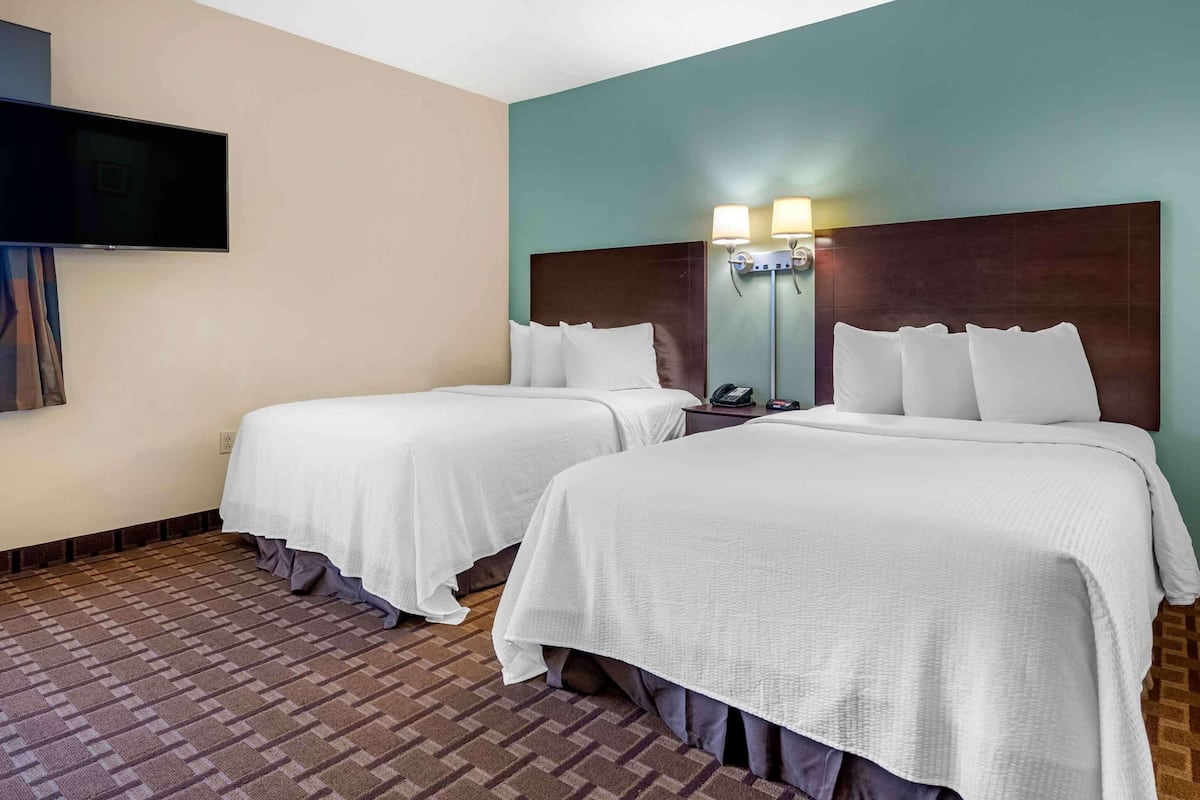 Habitación de hotel con dos camas, un televisor de pantalla plana montado en la pared y una mesita de noche con teléfono y lámpara.