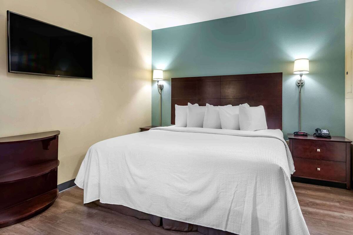 Habitación de hotel con cama, lámparas de noche, televisor de pantalla plana, cómoda y mesita de noche con teléfono.