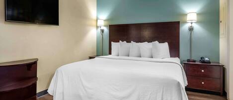 A hotel room with a bed, bedside lamps, a flat-screen TV, a dresser, and a nightstand with a phone.