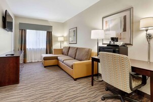 Habitación de hotel con sofá, escritorio, silla, televisión, cafetera y lámpara.