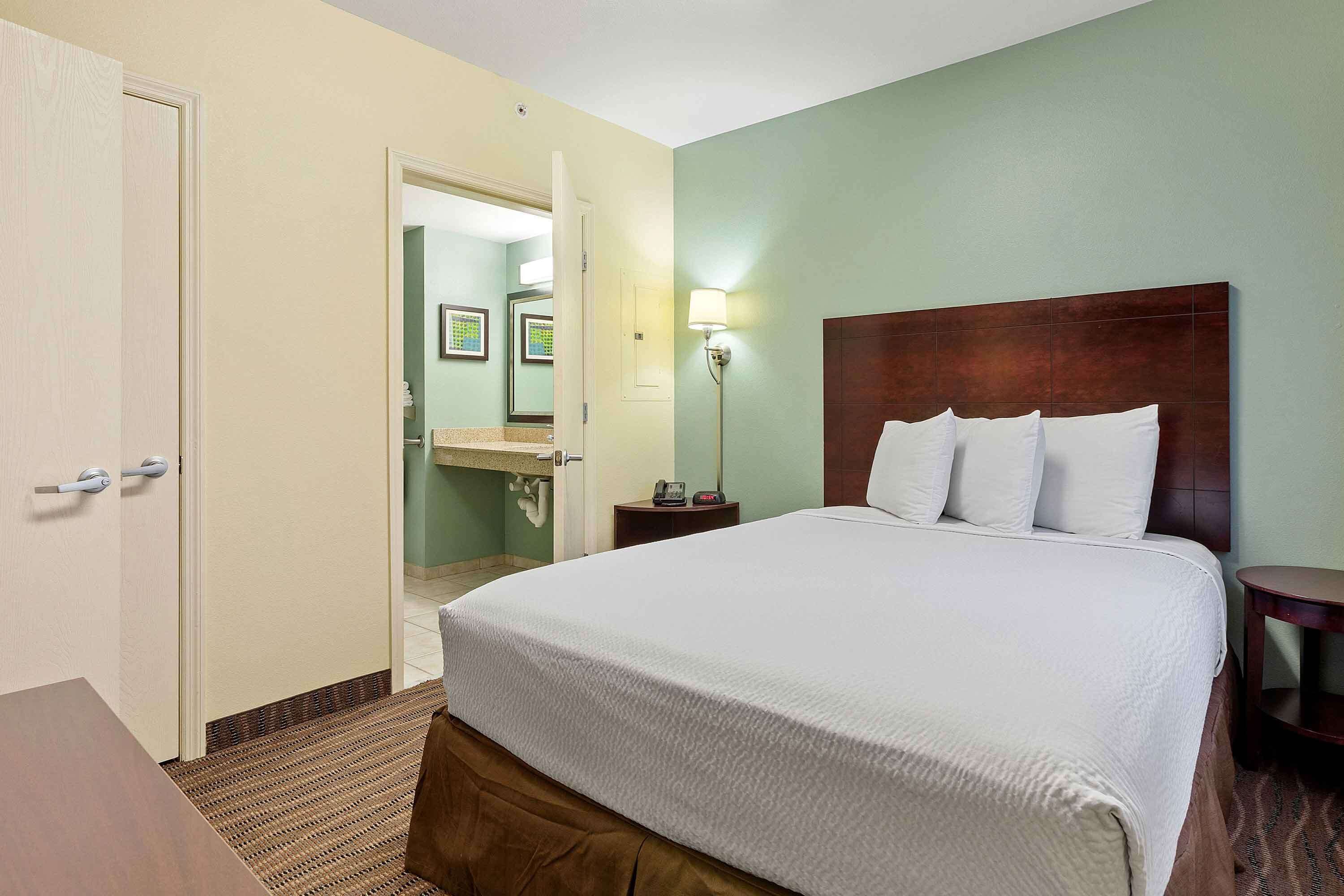 A hotel room with a large bed, a bedside table, a nightstand, a lamp, and a door leading to a bathroom.