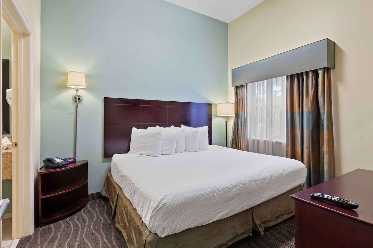 Habitación de hotel con cama, mesita de noche con teléfono, escritorio con control remoto y ventana con cortinas.