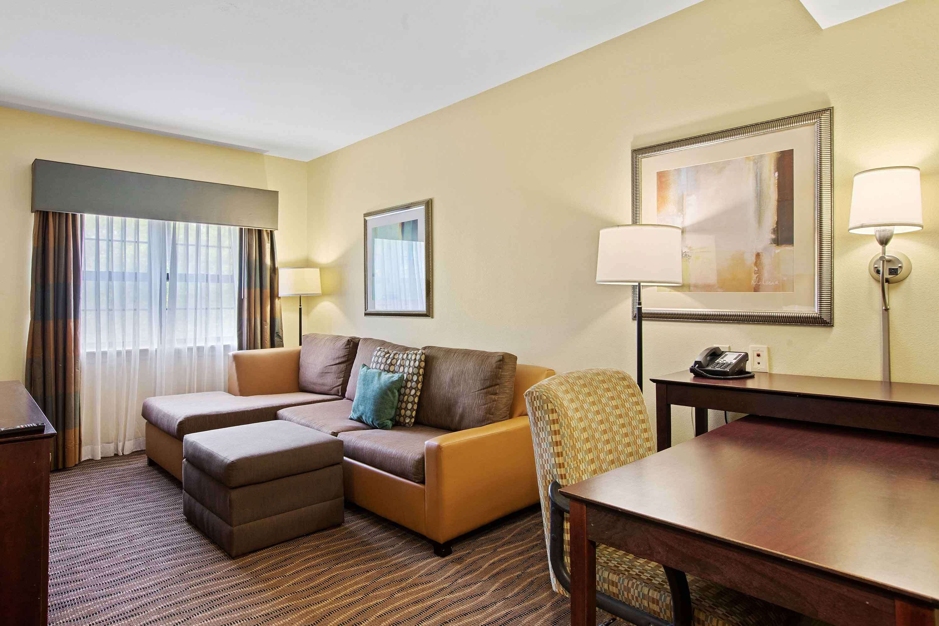 A hotel room with a sofa set, a dining table, a telephone, and a framed artwork on the wall.
