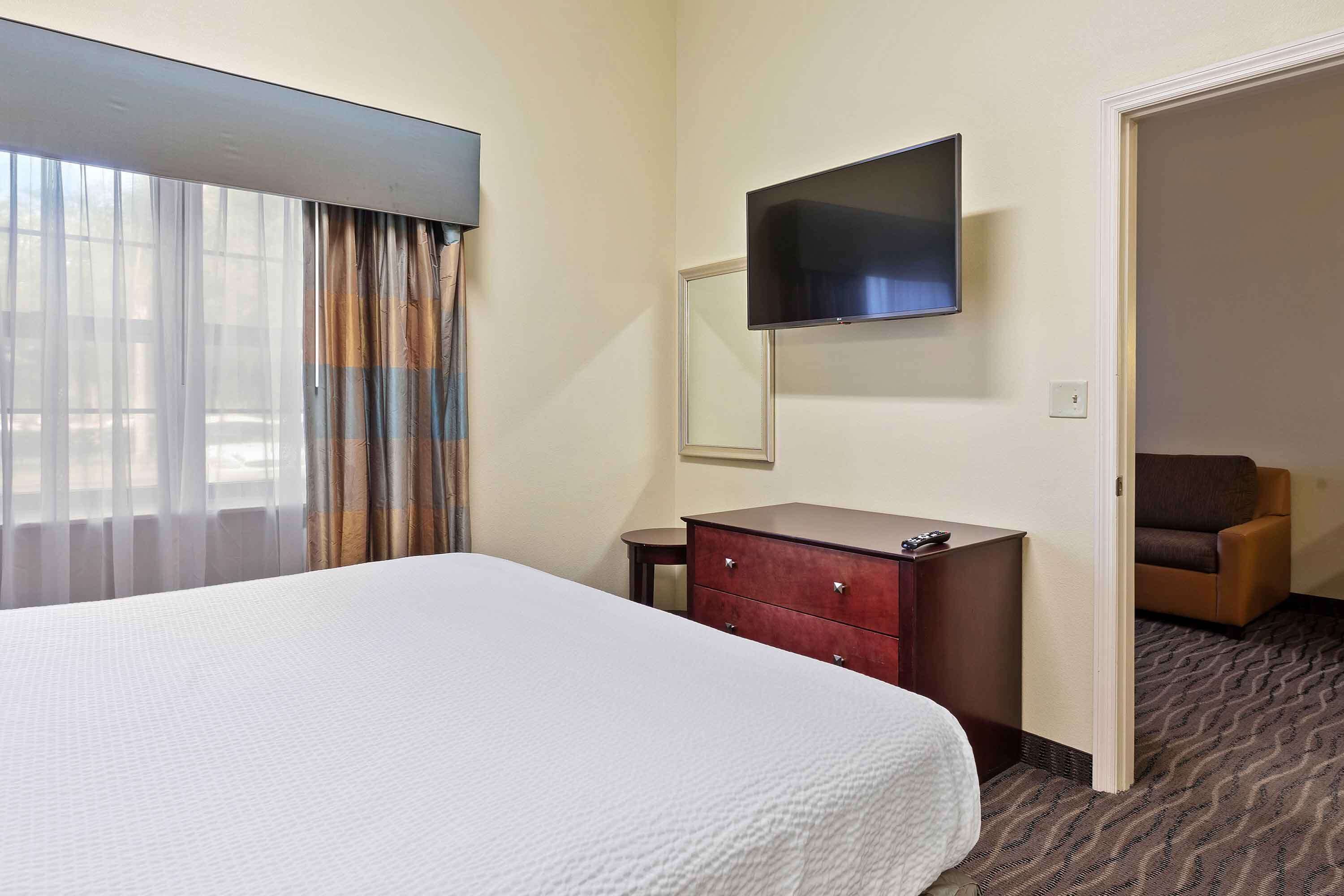 A hotel room with a large bed, a dresser, a television mounted on the wall, and a view through the window.