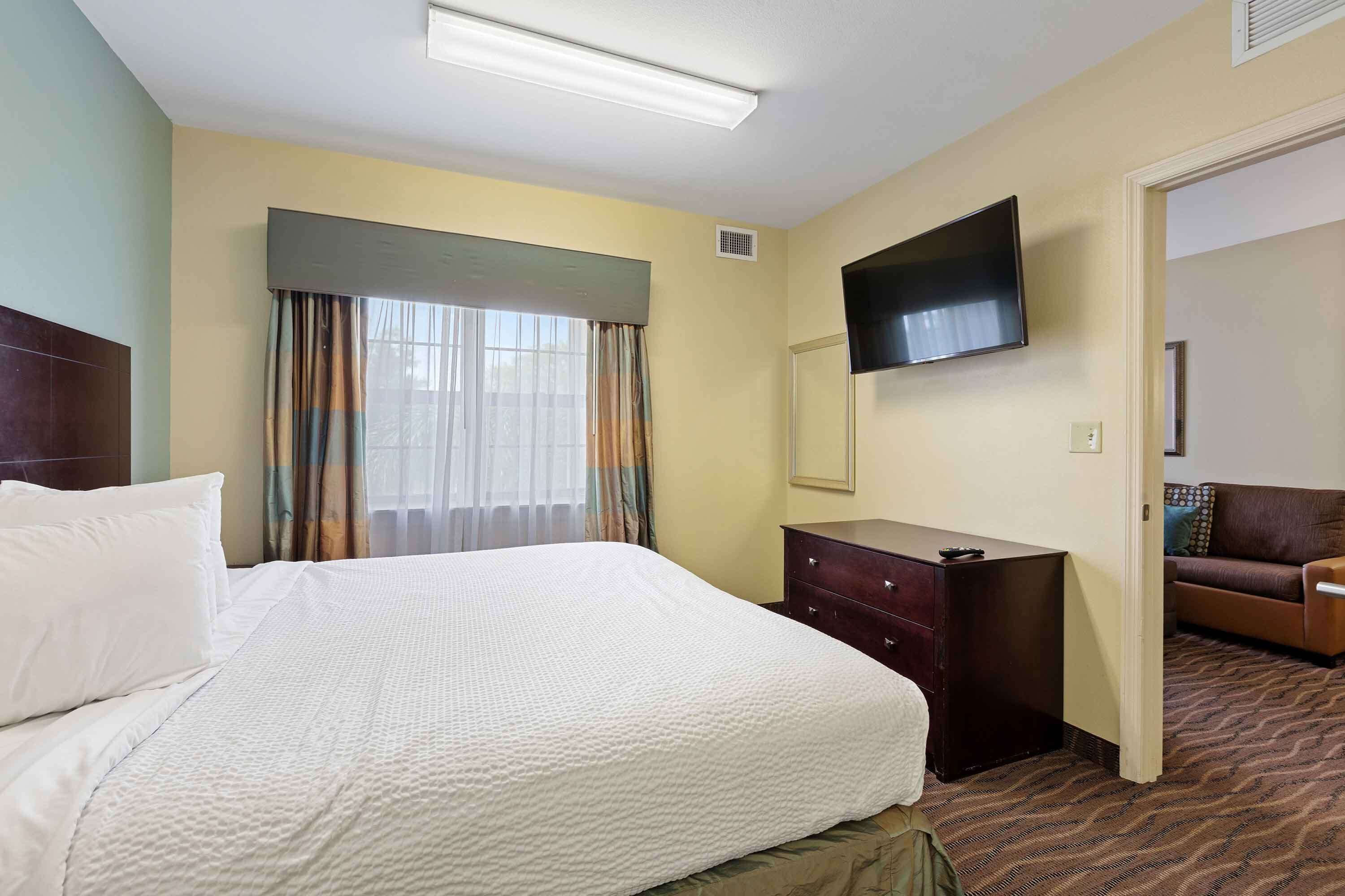 Une chambre d’hôtel avec un grand lit, une commode, un téléviseur fixé au mur et un canapé dans un coin.