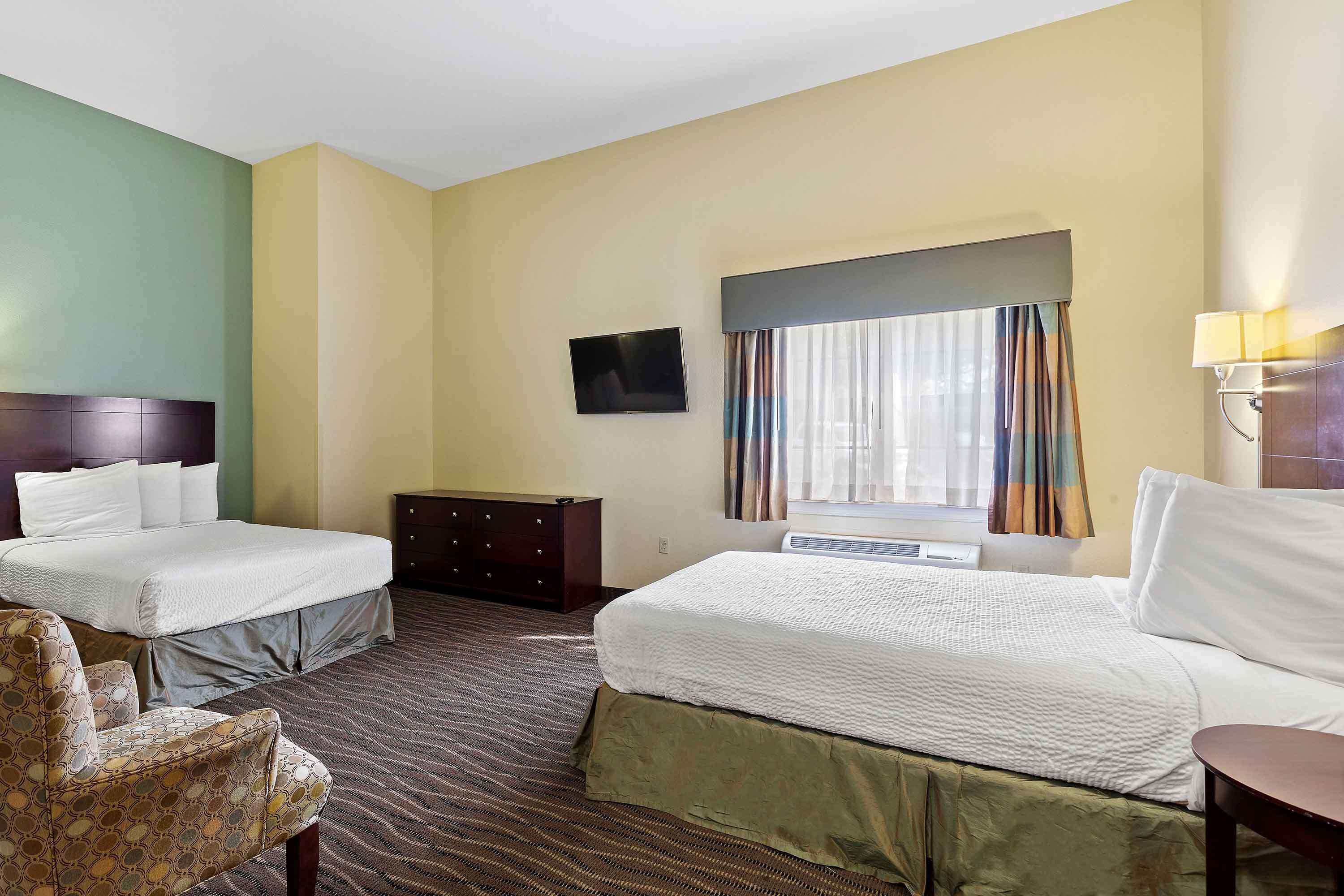 Una habitación de hotel con dos camas, un televisor, un aparador y una silla.