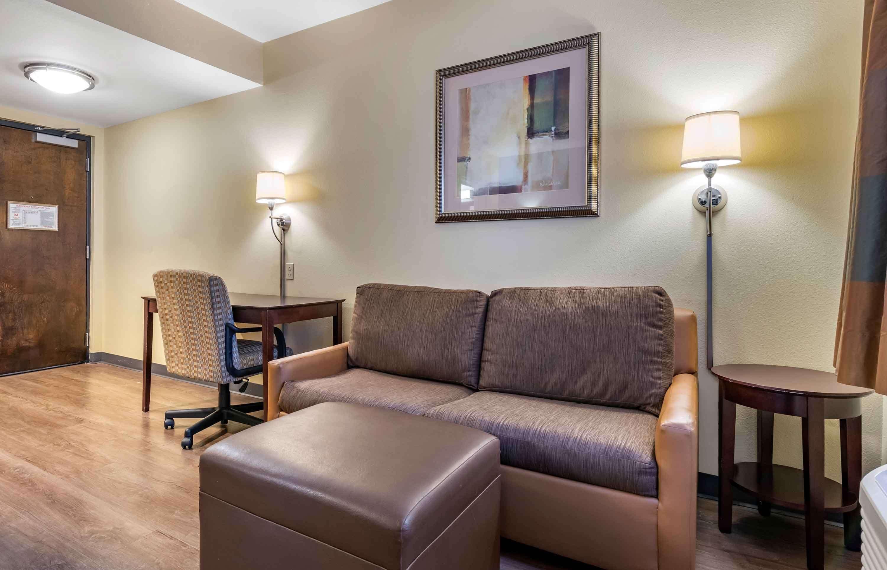A hotel room with a sofa, an ottoman, a chair, two side tables, and a framed picture on the wall.