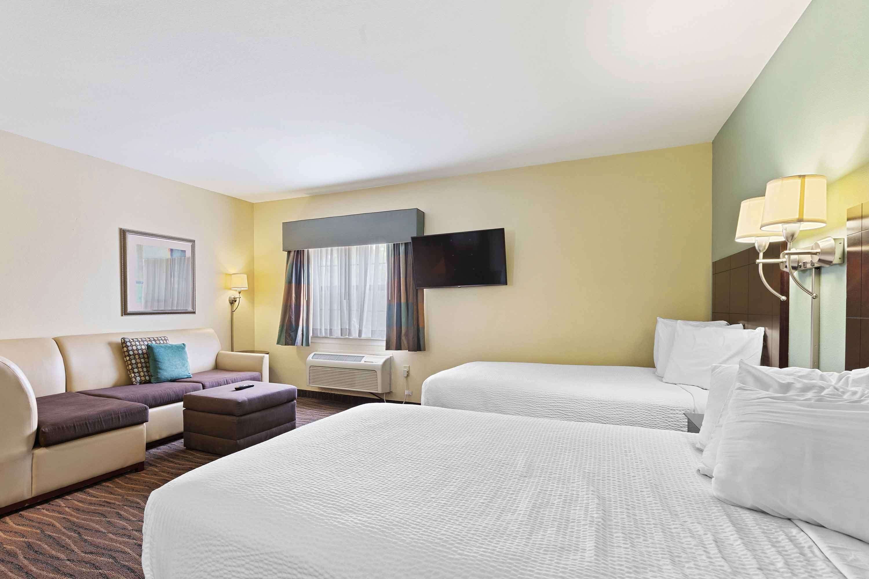 Habitación de hotel con dos camas, un sofá, una mesita, un televisor y una ventana con cortinas.
