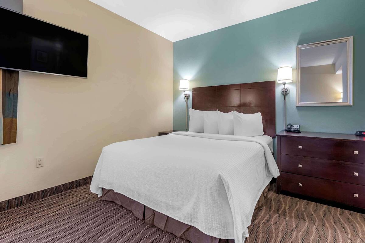 Habitación de hotel con cama, televisor de pantalla plana en la pared, cómoda y espejo.