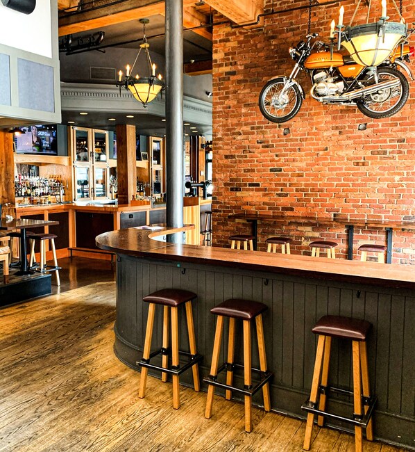 A bar area with stools, a brick wall, and a motorcycle mounted on the wall.