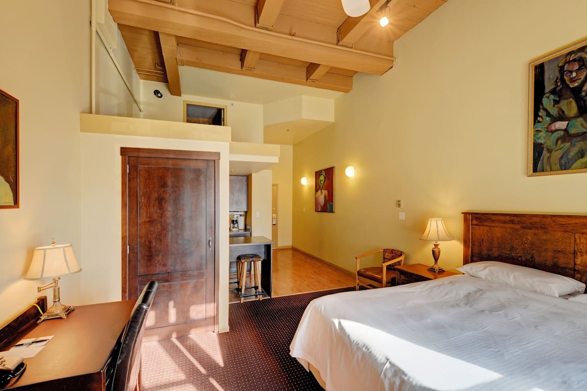 A hotel room with a bed, desk, chair, and a small kitchenette area.