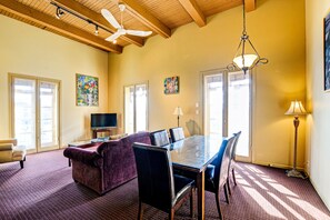 A spacious living room with a large dining table, comfortable seating, and a ceiling fan.
