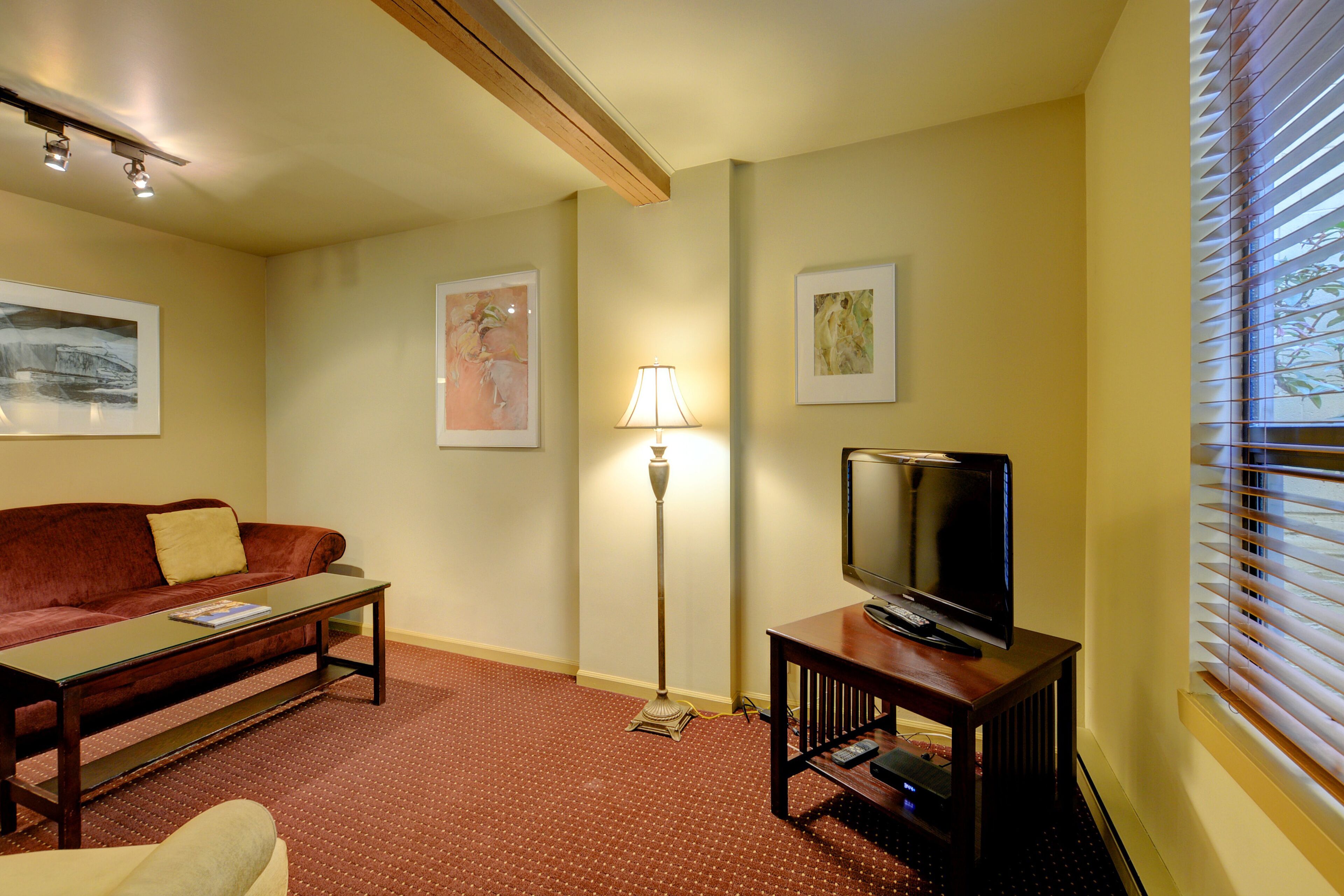 A living room with a sofa, coffee table, floor lamp, television, and artwork on the walls.