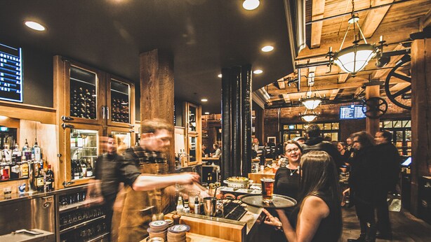 A bar with wooden interiors, a bartender, and patrons. - Swans Brewery, Pub and Hotel (Victoria)
