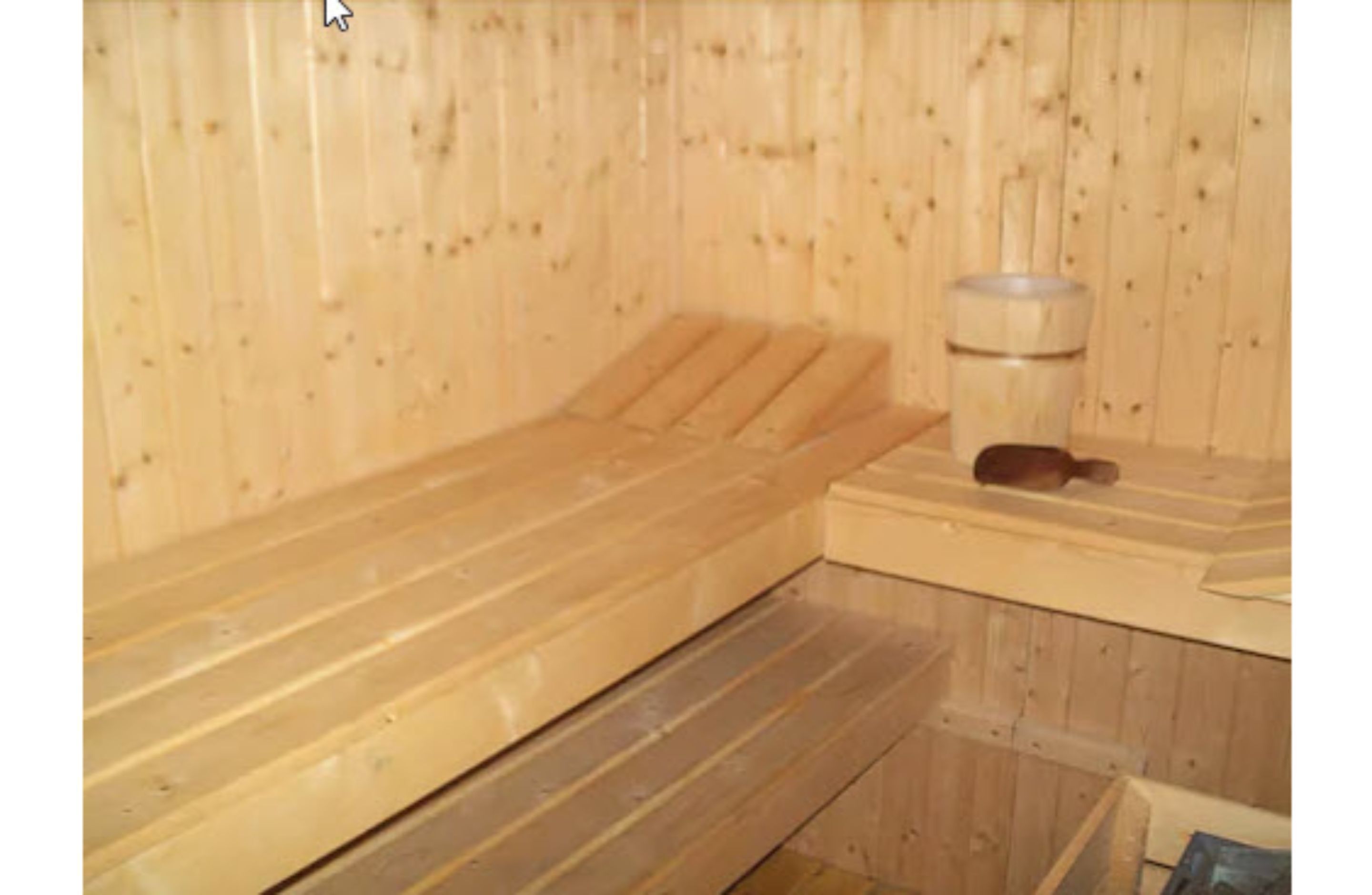 A sauna with wooden benches and a bench seat, a wooden wall, and a small table with a container.