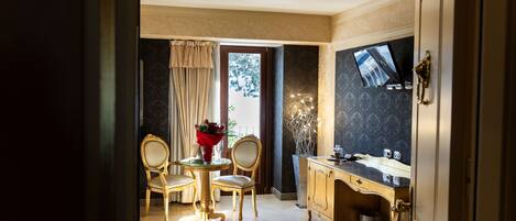 A hotel room with a dining area, a television, a cabinet, and a window with curtains.