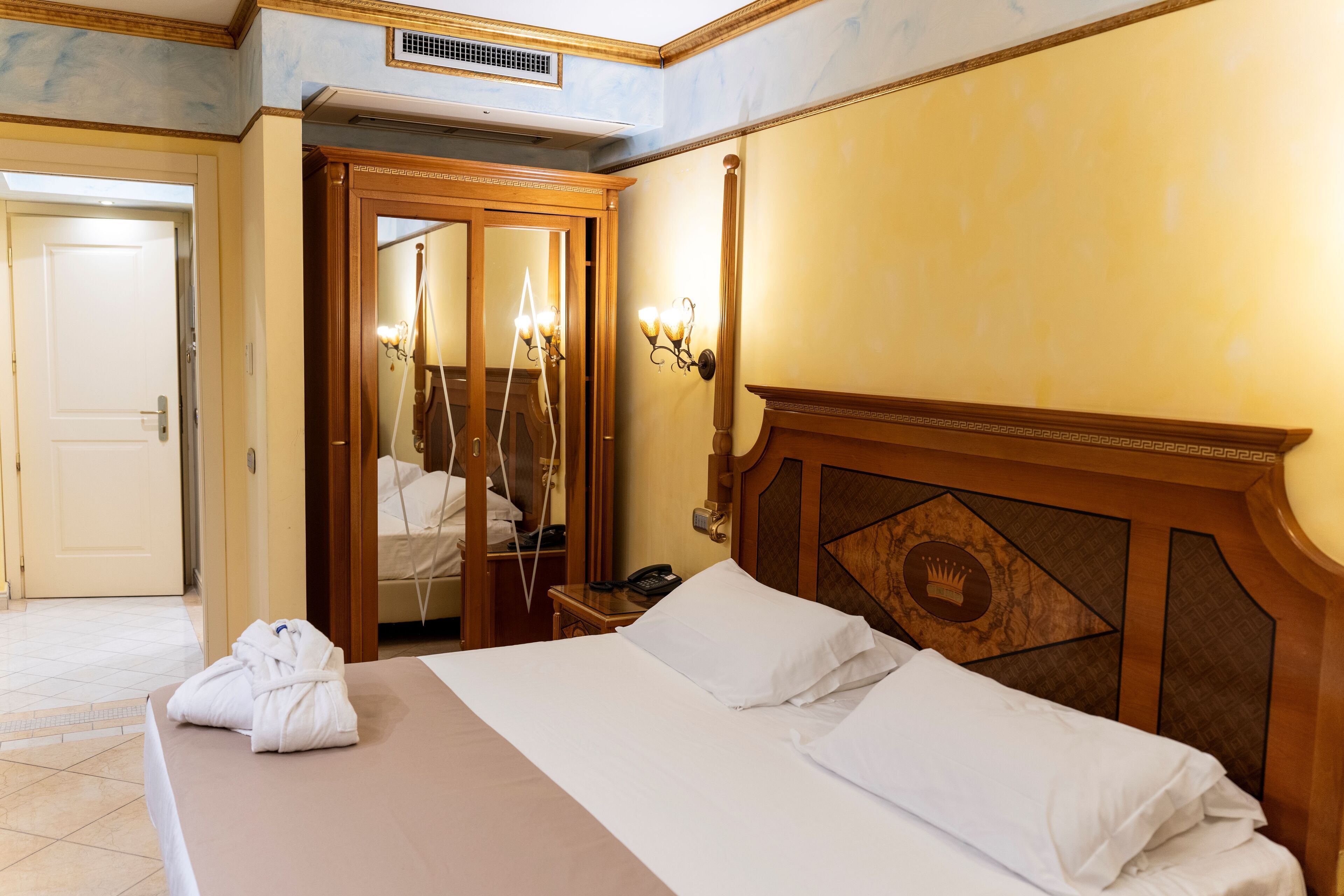 Hotelkamer met een bed, een houten hoofdbord, een spiegel, een nachtkastje en een badkamer zichtbaar door een open deur.