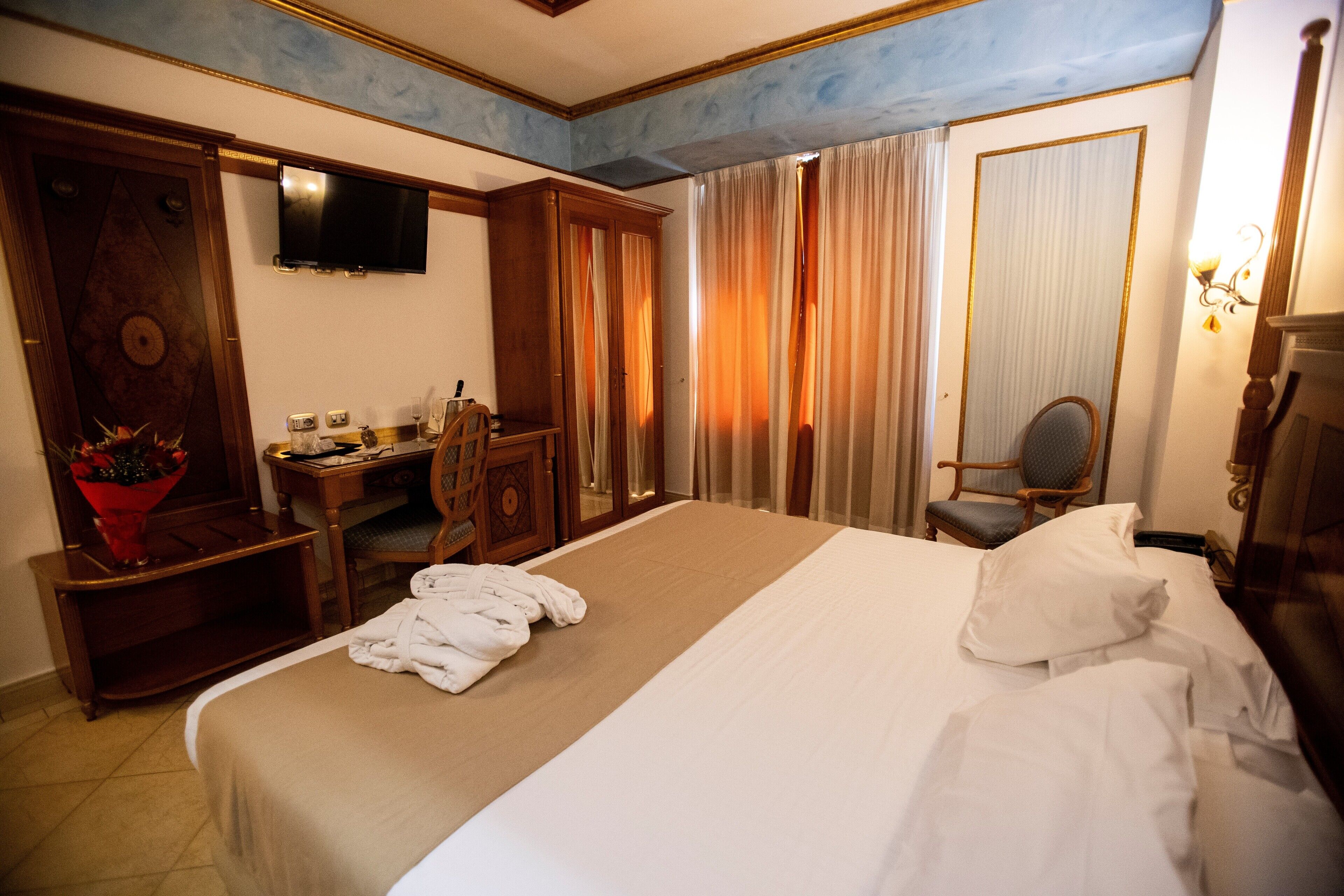 Una camera d'albergo con un letto grande, una scrivania con una sedia, una televisione a parete e un armadio.