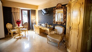 Quarto luxuoso com design clássico, apresentando um espelho grande e ornamentado, uma escrivaninha com cadeira e um espaço de estar com duas poltronas.