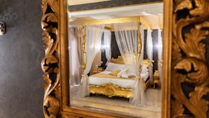 Um quarto luxuoso com uma cama de dossel, moldura dourada ornamentada e cortinas leves.