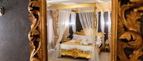 A luxurious bedroom with a four-poster bed, ornate gold frame, and sheer curtains.