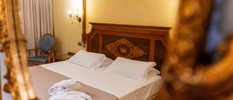 A hotel room with a large bed, a chair, a desk, and a wall-mounted lamp.