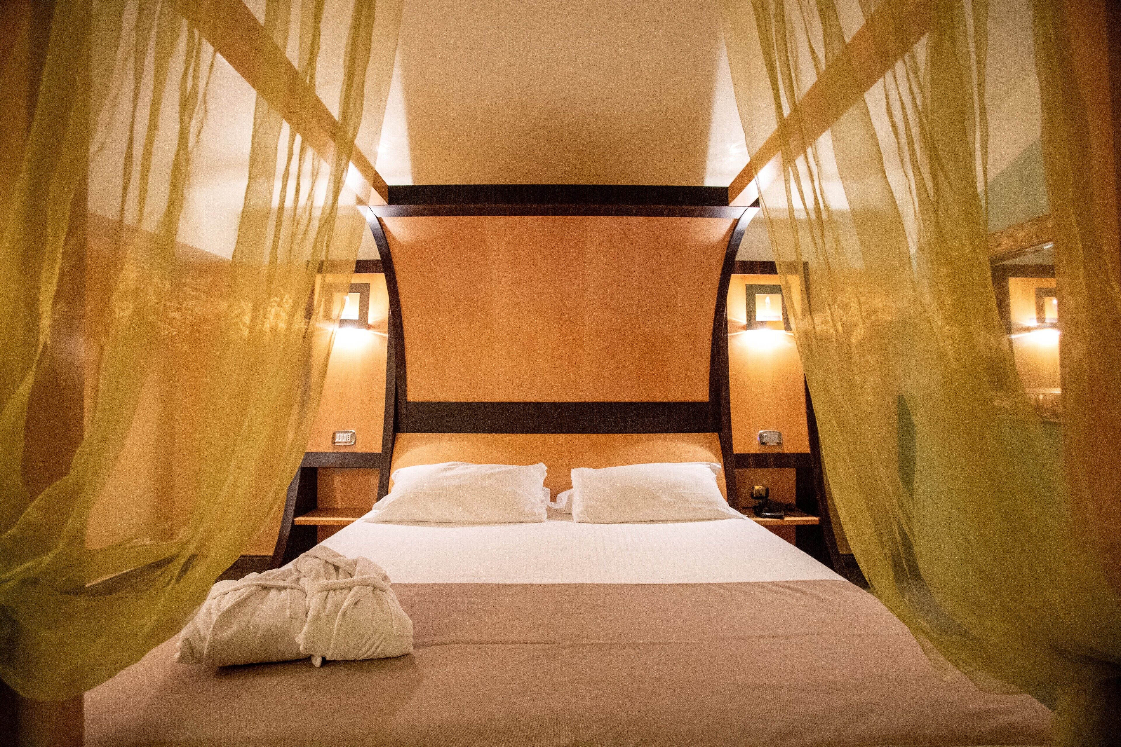 A neatly made bed with white linens, a bedside table with a lamp, and sheer curtains.