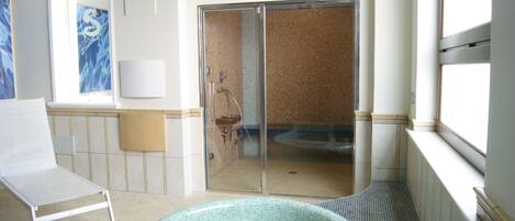 A spa room with a glass-enclosed shower, a small sink, and a lounge chair.