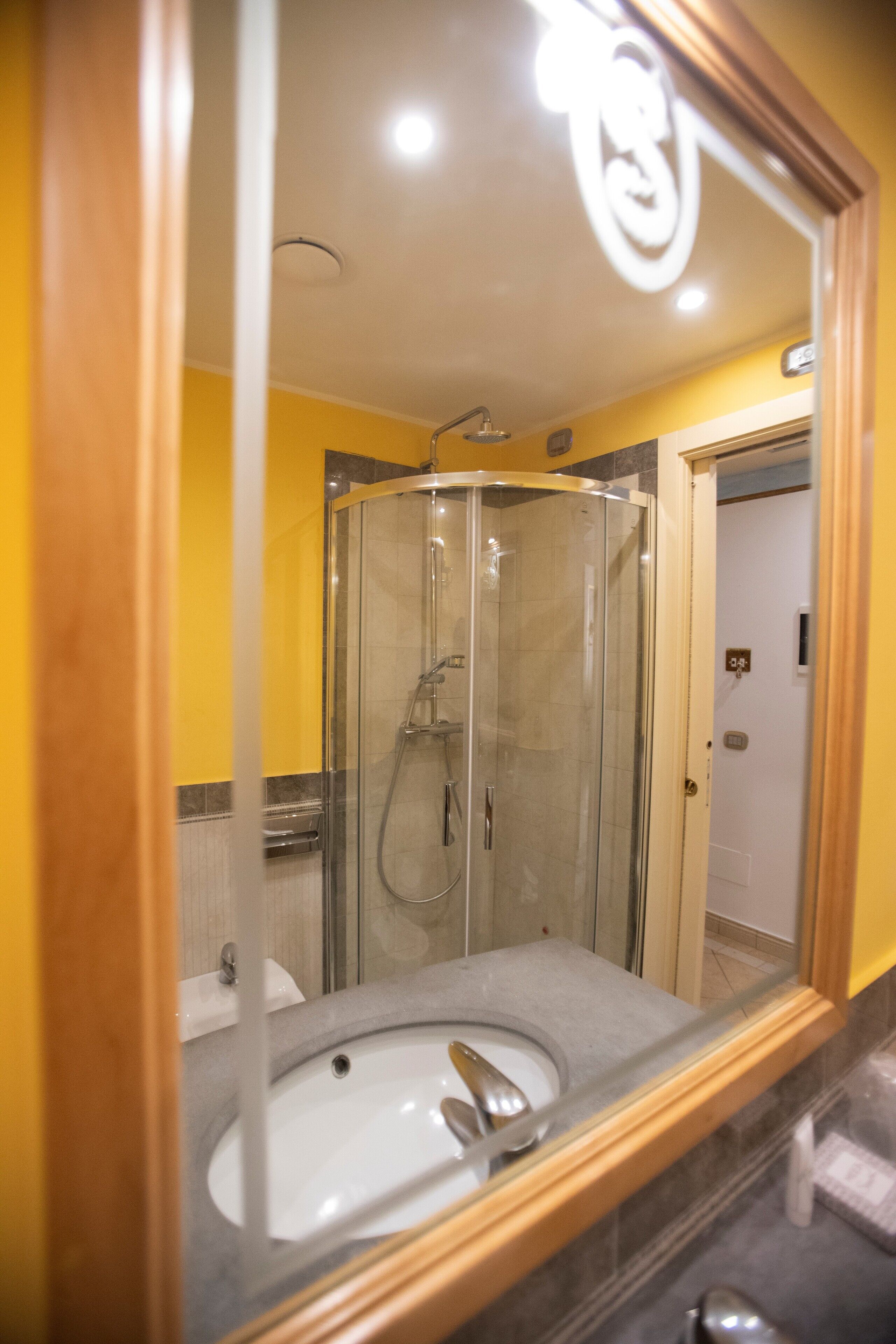 A bathroom with a glass-enclosed shower, a sink, and a mirror with a wooden frame.