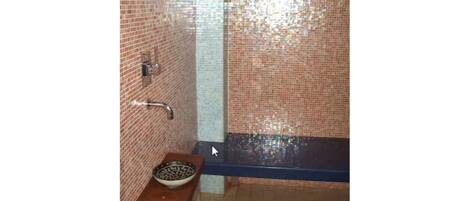 A bathroom with a tiled wall, a sink with a bowl, and a shower area.
